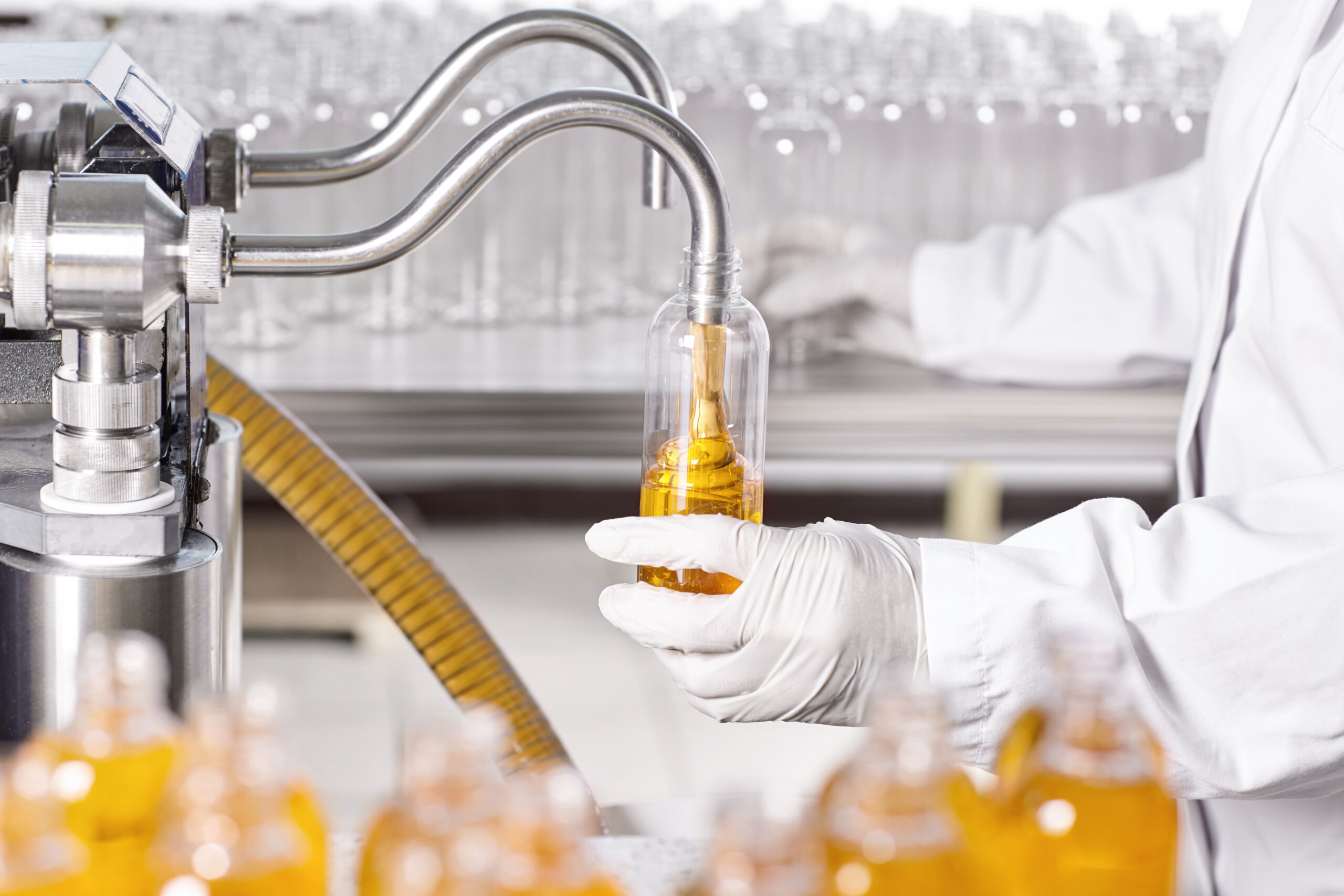 Production process of cosmetics in laboratory. Laboratory scientist dressed in hospital gown and gloves working at lab holding glassware with yellow liquid. Laboratory,scientific research concept.